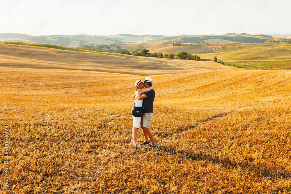 Portrait of middle age couple kissing each other at yellow field during summer holidays at Tuscany, Italy. Senior couple wear stylish clothes and hat during sunset. Portrait of middle age couple kissing each other at yellow field during summer holidays at Tuscany, Italy. Senior couple wear stylish clothes and hat during sunset.