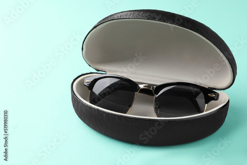 Stylish sunglasses in black leather case on light blue background