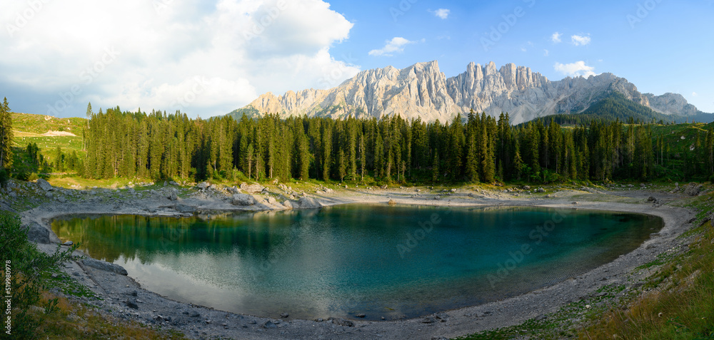 Stunning panoramic view of Carezza Lake (Lago di Carezza) with its emerald green waters, beautiful trees and mountains in the distance during a dramatic sunset. Stunning panoramic view of Carezza Lake (Lago di Carezza) with its emerald green waters, beautiful trees and mountains in the distance during a dramatic sunset.