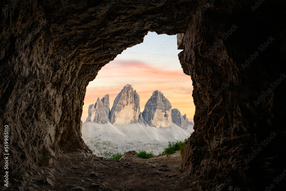 Stunning view of the Three Peaks of Lavaredo, (Tre cime di Lavaredo) during a beautiful sunset framed by a cave. The Three Peaks of Lavaredo are the undisputed symbol of the Dolomites, Italy.