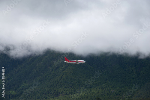 Airplane flying through the clouds over the pine forest covered mountains