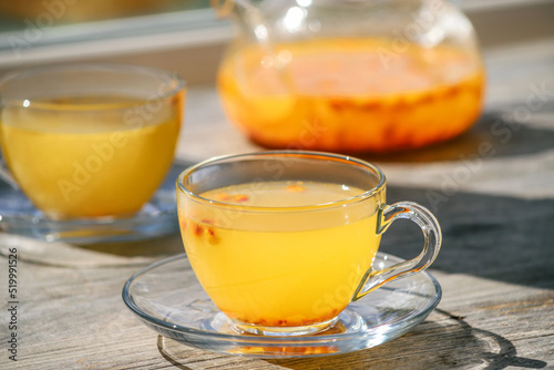 Sea buckthorn tea in glass cups and teapot on a wooden windowsill. Healthy vitamin drink, close up