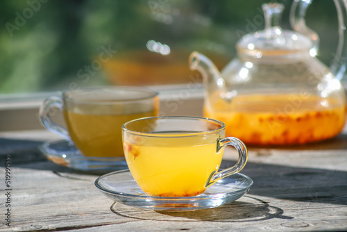 Sea buckthorn tea in glass cups and teapot on a wooden windowsill. Healthy vitamin drink