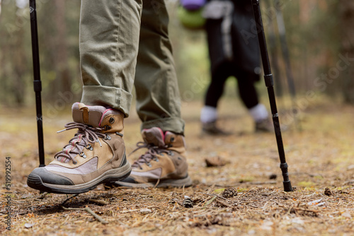 Close up of woman's rugged hiking boots and jeans on a leaf covered forest trail. Hiker in the middle of image with forest behind her.