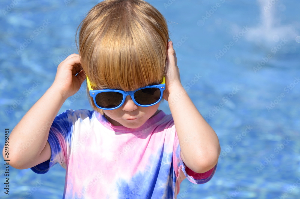 Happy child on sunglasses near pool. Smiling boy having fun outdoor in resort. Summer vacation.Summertime kids weekend. Funny boy at aquapark Happy child on sunglasses near pool. Smiling boy having fun outdoor in resort. Summer vacation.Summertime kids weekend. Funny boy at aquapark