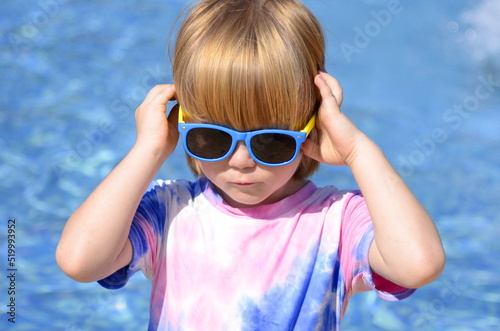 Happy child on sunglasses near pool. Smiling boy having fun outdoor in resort. Summer vacation.Summertime kids weekend. Funny boy at aquapark
