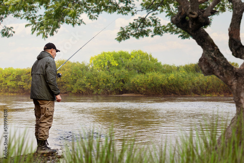 A fisherman in a jacket with a fishing rod stands on the bank of the river. Fishing in the river. Fisherman with a fishing rod on the river bank. Fishing, spinning reel, fish.