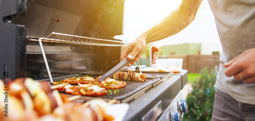 Young man grilling some kind of meats on the gas grill during lovely summer time, food concept