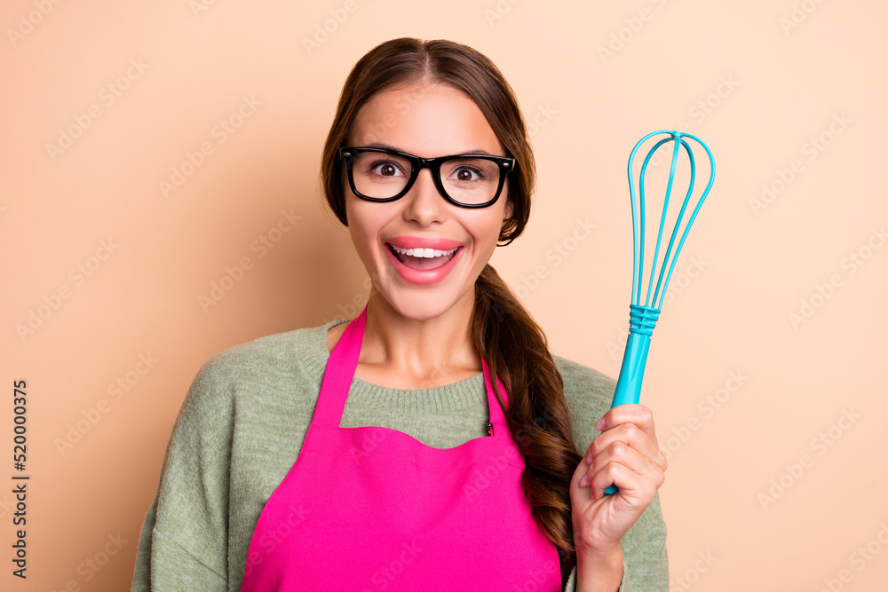 Photo of sweet excited girl dressed pink apron eyewear rising cooking utencil isolated beige color background Photo of sweet excited girl dressed pink apron eyewear rising cooking utencil isolated beige color background