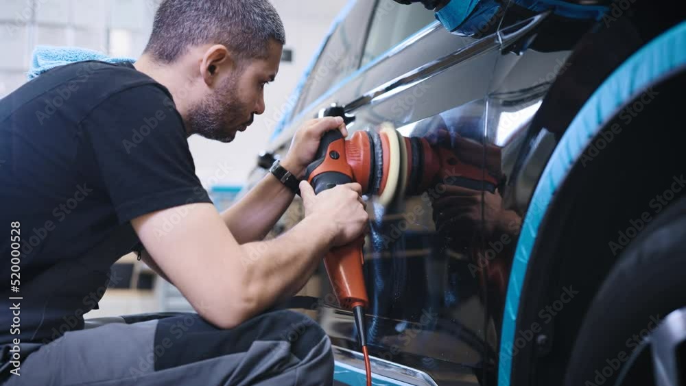 An experienced detailing studio worker polishing a car. An experienced detailing studio worker polishing a car.