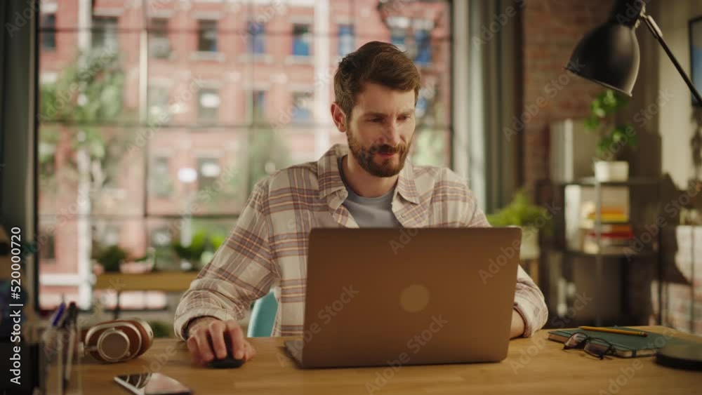 Stylish Bearded Young Adult Man Using Laptop Computer in Creative Loft Office Space. Happy Specialist in Checkered Shirt Working Remotely on Agency Projects from Home. Arc Shot. Stylish Bearded Young Adult Man Using Laptop Computer in Creative Loft Office Space. Happy Specialist in Checkered Shirt Working Remotely on Agency Projects from Home. Arc Shot.