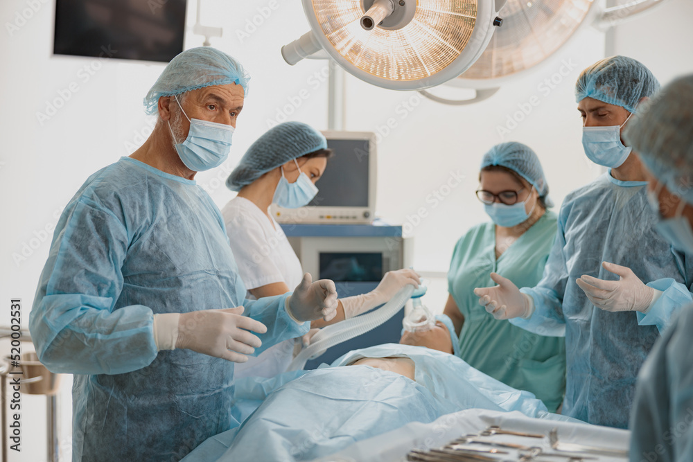 Concentrated surgical team working with a patient in an operation room of modern clinic Concentrated surgical team working with a patient in an operation room of modern clinic