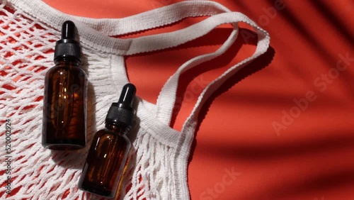 Cosmetic bottles with oil and cloth shopping bag. Red background with daylight and palm shadow. Sun protection lotion, sunscreen. Summer skin care concept with spf.