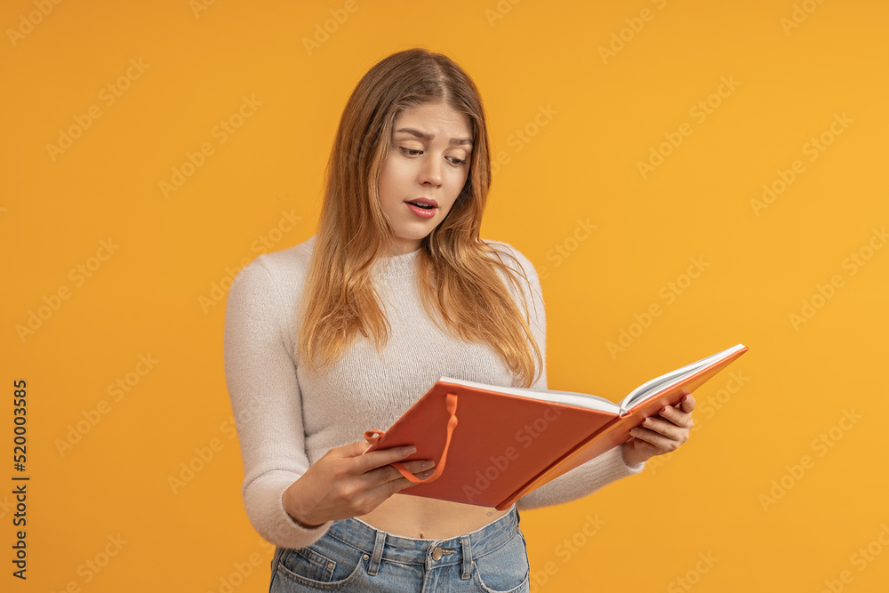 A young girl with long hair, opened a notebook or accounting book. She is discouraged. The girl doesn't like what she sees. The concept of mixed feelings. A young girl with long hair, opened a notebook or accounting book. She is discouraged. The girl doesn't like what she sees. The concept of mixed feelings.