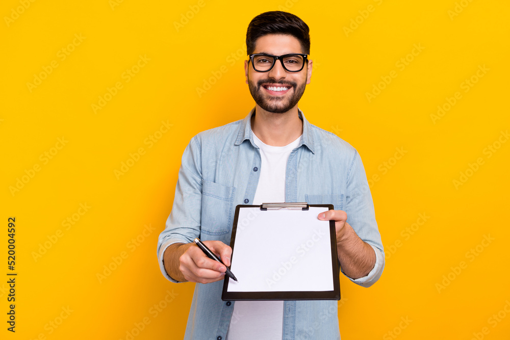Photo of young guy smiling holding notepad pen waiting you signature write for new delivery isolated on yellow color background Photo of young guy smiling holding notepad pen waiting you signature write for new delivery isolated on yellow color background