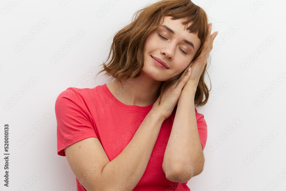 a gentle, relaxed, sleepy woman stands in a red T-shirt on a white background and holds her hands folded in her palms under her head, closing her eyes a gentle, relaxed, sleepy woman stands in a red T-shirt on a white background and holds her hands folded in her palms under her head, closing her eyes