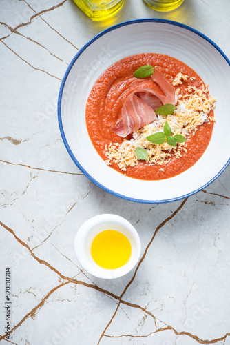 Plate of spanish salmorejo or tomato cream-soup with jamon and chicken egg, flat lay on a light-beige stone background, vertical shot with space photo