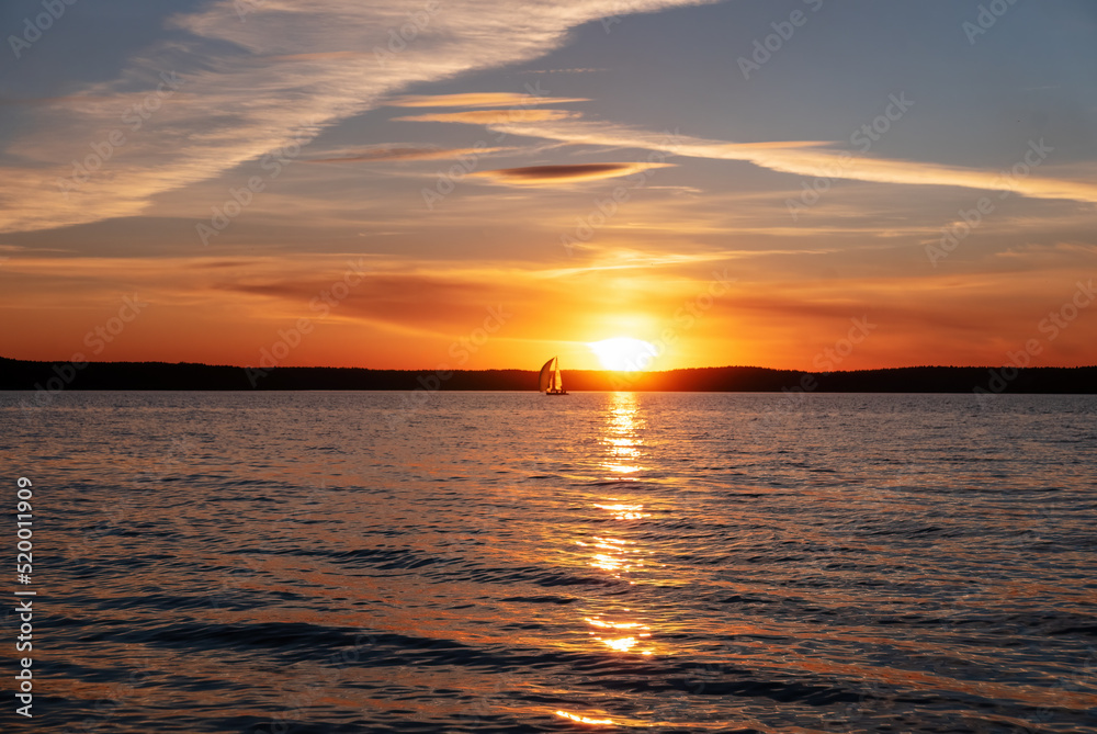 Peaceful sunset on the sea. Sailing yacht on the background of the setting sun. Focus on the foreground