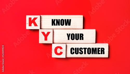 On a bright red background, wooden cubes and blocks with the text KYC KNOW YOUR CUSTOMER. Manufacturing of wooden toys.
