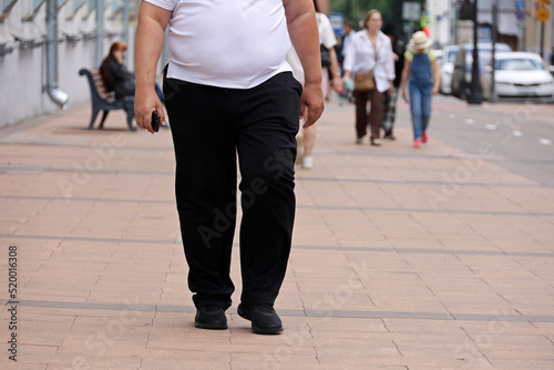 Fat man walking on city street on people background at summer. Concept of overweight, body positive