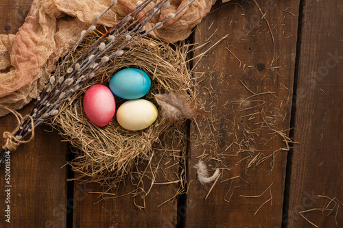 Painted Easter chicken eggs in a nest and willow branches. Holiday Easter concept background. High quality photo