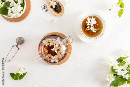 tea composition on a white background. glass teapot with jasmine tea, white forfor cup of tea, strainer, dry tea leaves. top view.
