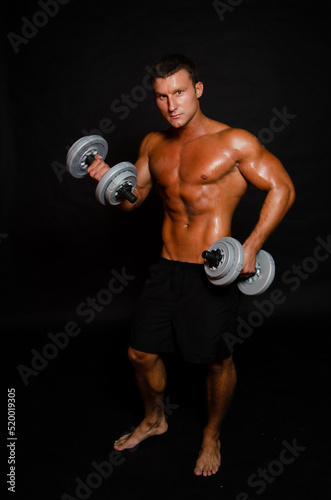 Young attractive sportsman with dumbbells. Male athletic body. 