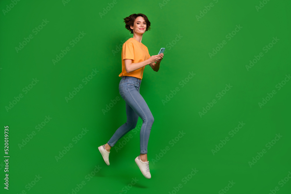 Full body profile photo of active charming person run jump hold telephone isolated on green color background Full body profile photo of active charming person run jump hold telephone isolated on green color background