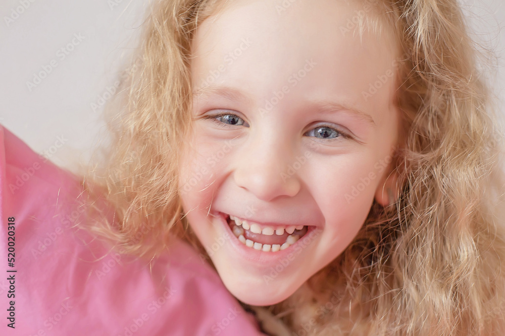 close-up portrait toothy smile cute blonde girl with curly hair hugs a pink pillow at home on the bed close-up portrait toothy smile cute blonde girl with curly hair hugs a pink pillow at home on the bed