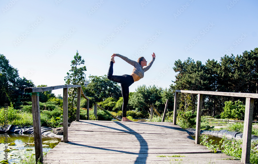 Fototapeta premium woman practicing yoga in the park on old bridge in summer sunny morning