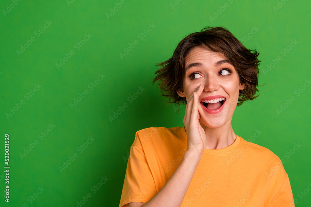 Photo of excited shiny young lady wear orange outfit arm lips looking empty space isolated green color background Photo of excited shiny young lady wear orange outfit arm lips looking empty space isolated green color background
