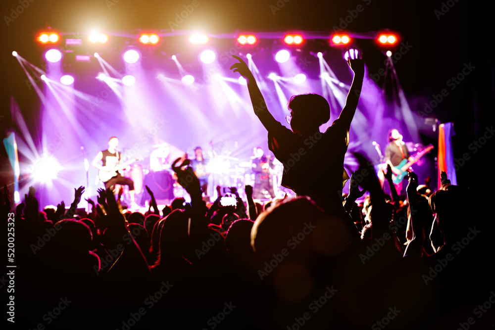 Concert hall with a lit stage and people silhouettes during a concert.