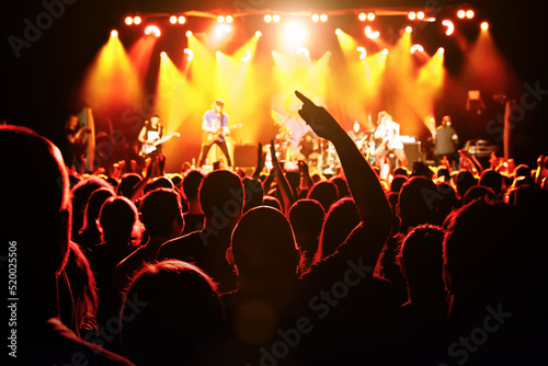 The man with raised hands during the music concert. Crowd and stage light in a concert hall.