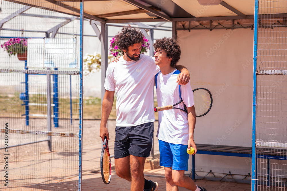 Fototapeta premium Charismatic and good looking father and son shaking hands before start to play the professional tennis match outdoor on the tennis clay court
