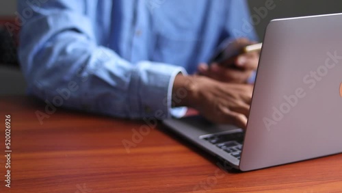 Man reading news on smartphone in social networks and using laptop computer while sitting at his desk.