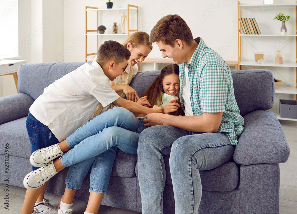 Kids and parents having fun. Happy funny family playing together. Cheerful mother, father and children playing on comfortable modern sofa at home, tickling each other and laughing