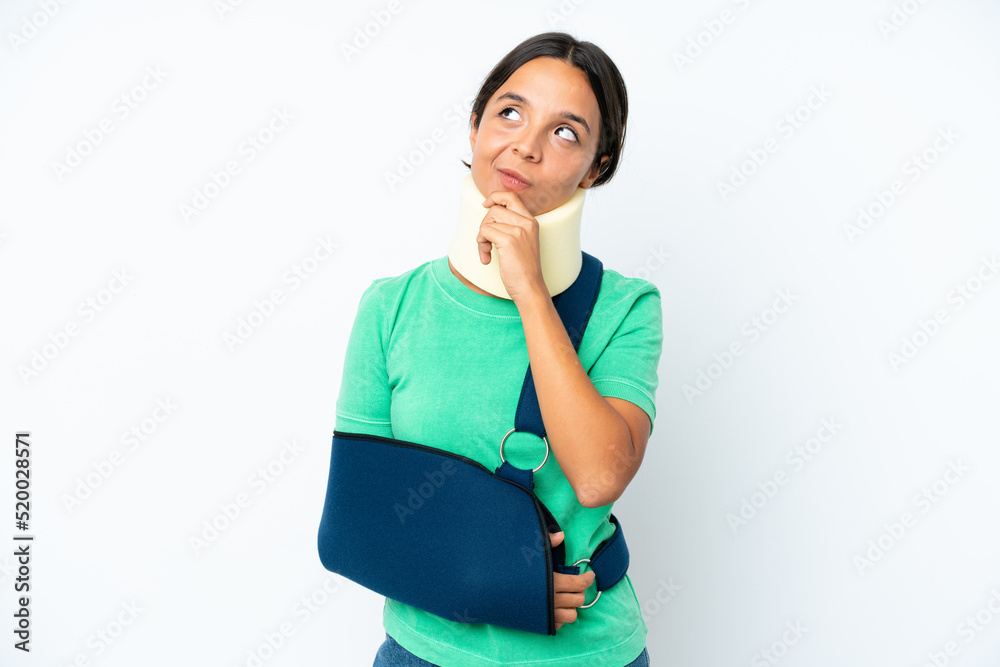 Young hispanic woman wearing a neck brace and sling isolated on white background having doubts while looking up Young hispanic woman wearing a neck brace and sling isolated on white background having doubts while looking up