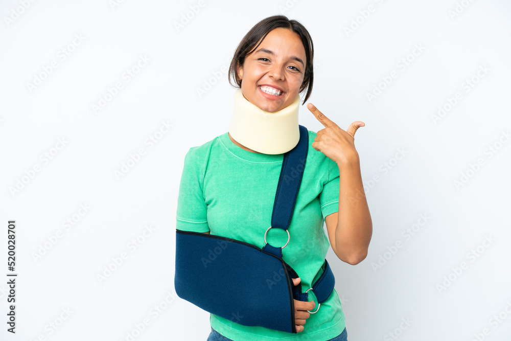 Young hispanic woman wearing a neck brace and sling isolated on white background giving a thumbs up gesture