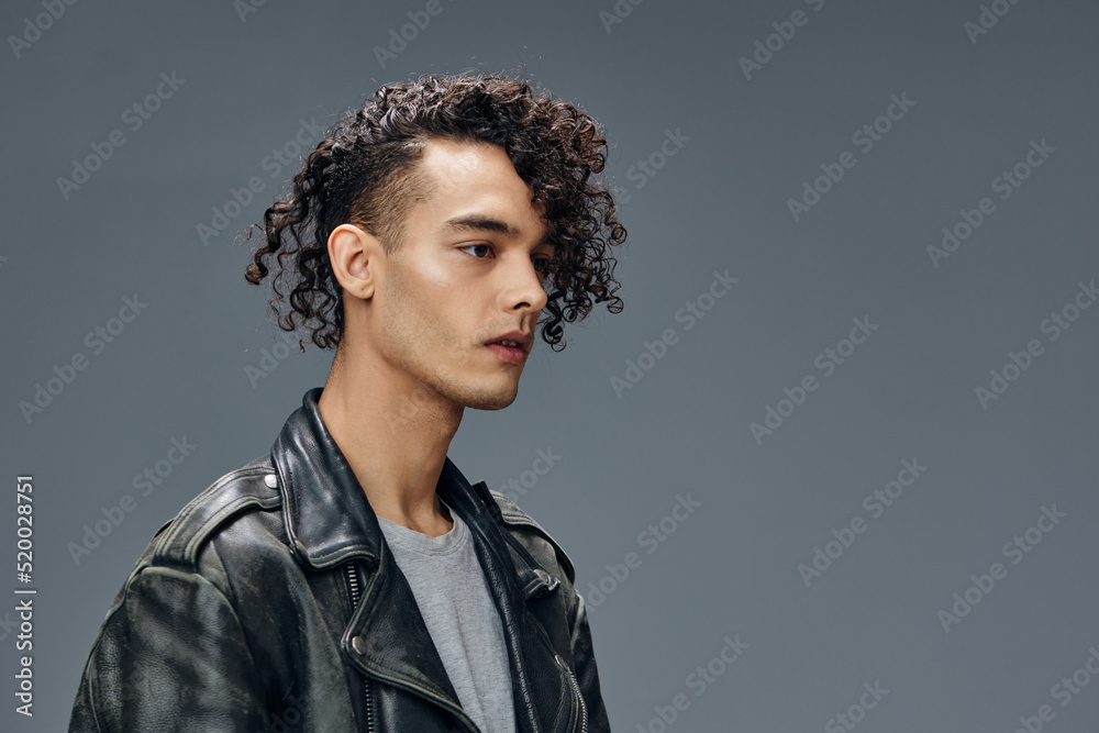 Pensive handsome stylish tanned curly man leather jacket looks aside posing isolated on over gray studio background. Cool fashion offer. Huge Seasonal Sale New Collection concept. Copy space for ad Pensive handsome stylish tanned curly man leather jacket looks aside posing isolated on over gray studio background. Cool fashion offer. Huge Seasonal Sale New Collection concept. Copy space for ad