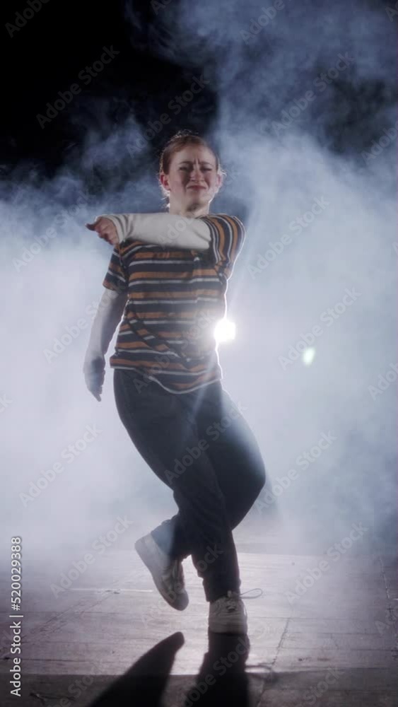 Vertical video of a Young female dancer performing hip hop dance in slow motion with light and smoke background Vertical video of a Young female dancer performing hip hop dance in slow motion with light and smoke background