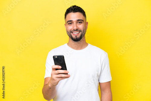 Young Arab handsome man isolated on yellow background using mobile phone