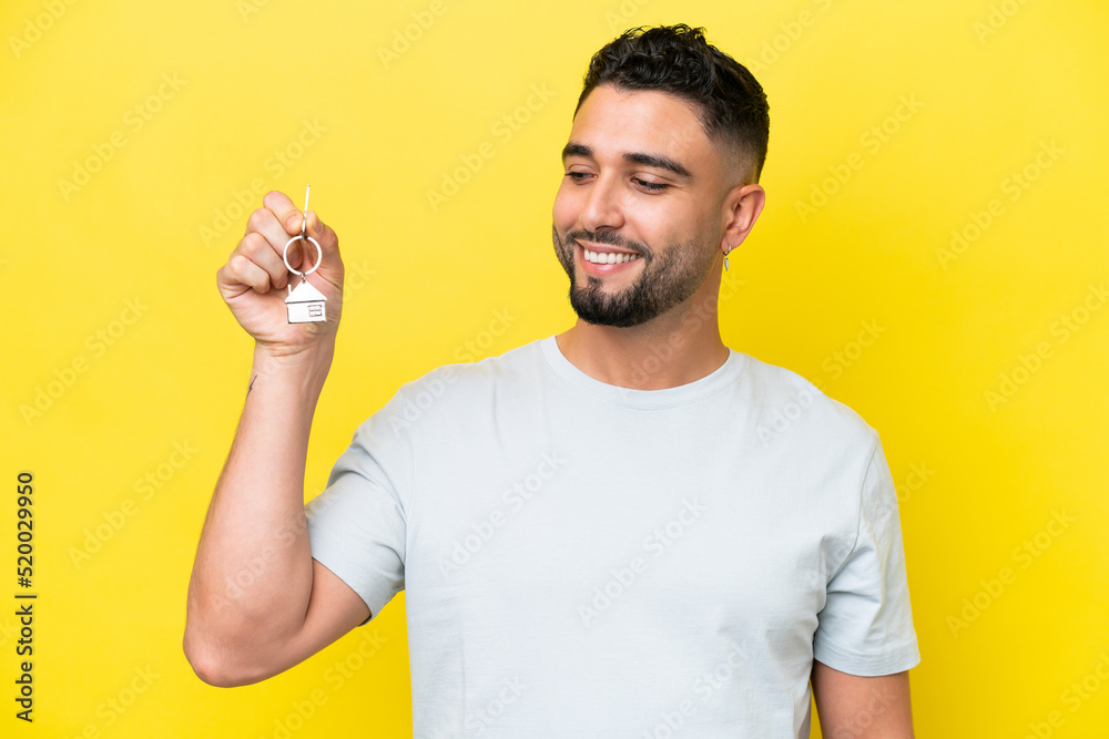 Young Arab man holding home keys isolated on yellow background with happy expression Young Arab man holding home keys isolated on yellow background with happy expression