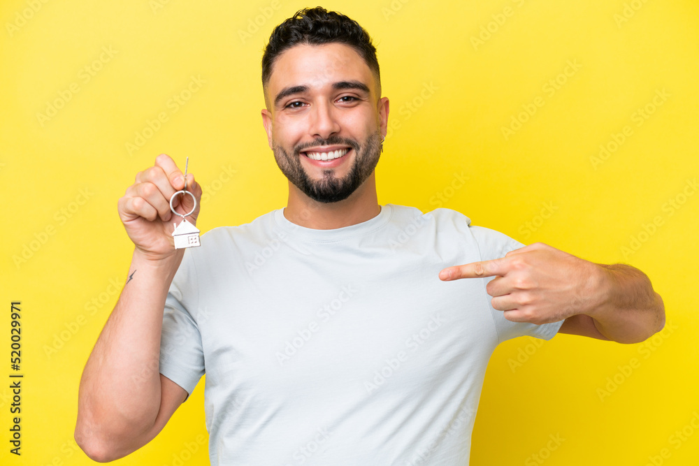 Young Arab man holding home keys isolated on yellow background with surprise facial expression Young Arab man holding home keys isolated on yellow background with surprise facial expression