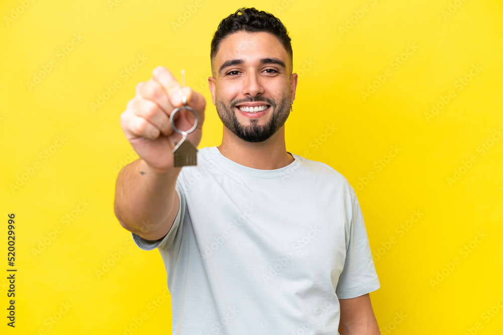Young Arab man holding home keys isolated on yellow background with happy expression Young Arab man holding home keys isolated on yellow background with happy expression