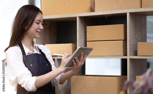 Young attractive asian woman owner startup business look at camera work happy with box at home prepare parcel delivery in sme supply chain, procurement, omnichannel or coronavirus quarantine concept.
