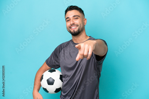 Fototapeta Naklejka Na Ścianę i Meble -  Young Arab handsome man isolated on blue background with soccer ball and pointing to the front