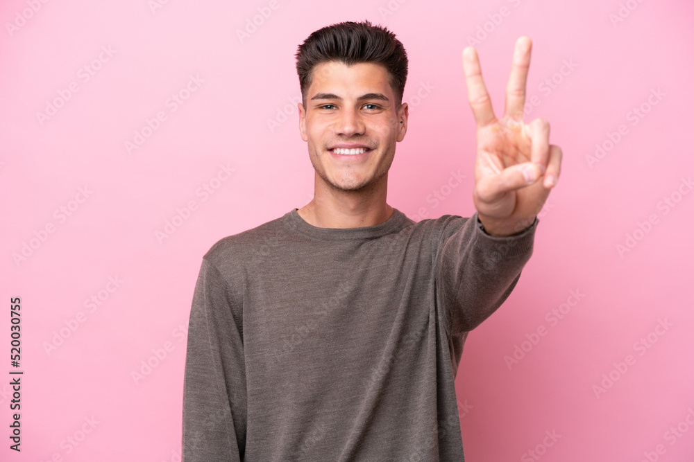 Young caucasian man isolated on pink background smiling and showing victory sign Young caucasian man isolated on pink background smiling and showing victory sign