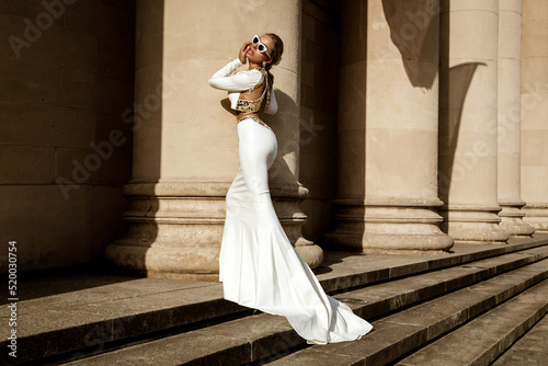 Elegant luxury fashion. Glamour, stylish elegant woman in long gown white dress is posing outdoor. Female model in amazing long dress in the park. Outdoor shoot. Vogue. Couture. photo