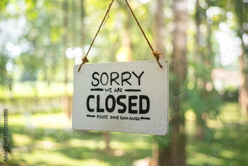 "Sorry, we are closed" wooden banner of cafe or restaurant, with background of outdoor environment. Sign and symbol object photo. © Nattawit
