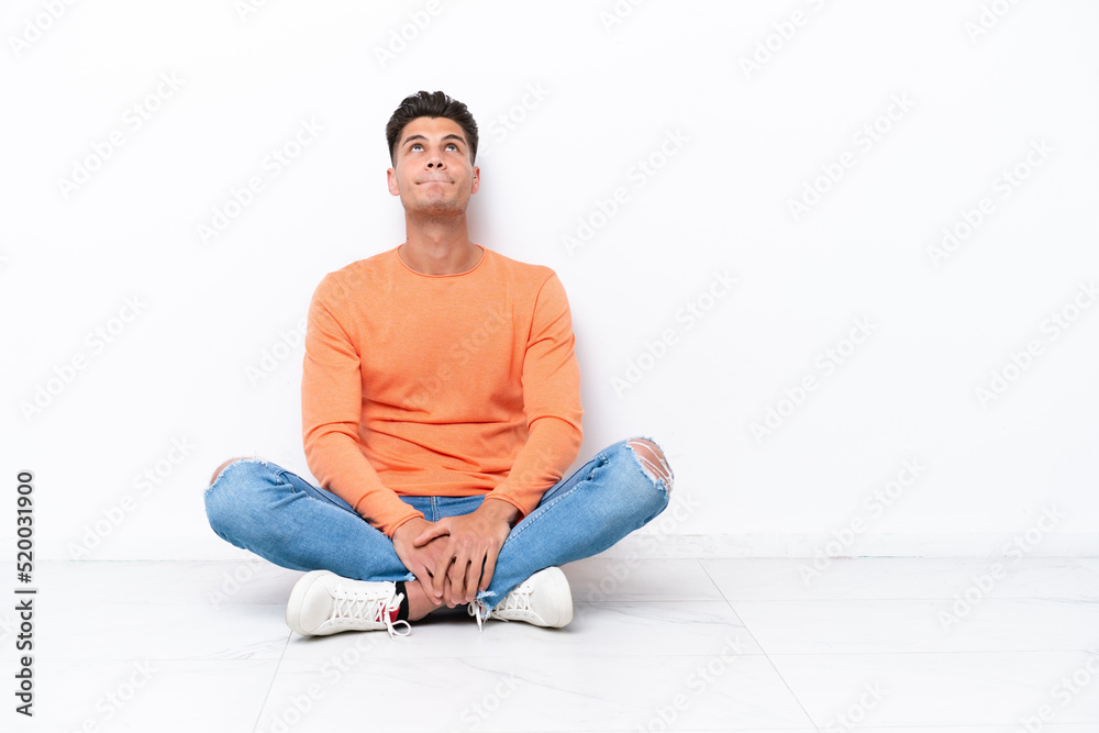 Young man sitting on the floor isolated on white background and looking up Young man sitting on the floor isolated on white background and looking up